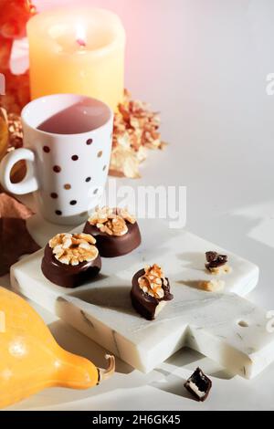 Schokoladen-Pralinen mit Walnussnüssen auf Marmor-Schneidebrett. Nahaufnahme von Süßigkeiten. Herbstarrangement mit Espresso-Kaffeetasse, Kerze, Kürbissen und trocken Stockfoto