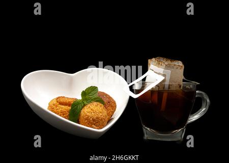 Brasilianische Gourmetgerichte und -Getränke servierten Brot und Käsebälle in einer herzförmigen Schüssel neben einer Tasse Kaffee mit Papierfilter Stockfoto