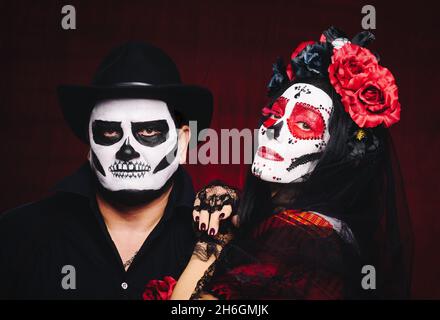 Schöne Frau mit einem Zuckerschädel Make-up mit einem Blumenkranz auf ihrem Kopf und einem Skelett Mann in einem schwarzen Hut Stockfoto