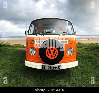 Vorderansicht eines klassischen Volkswagen Orange Wohnwagens am Strand mit dem VW-Abzeichen auf der Fahrzeugabdeckung Stockfoto