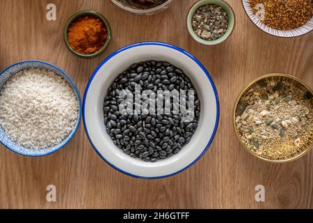 Weiße Schüssel mit schwarzen Bohnen, daneben eine Schüssel mit Reis, eine andere mit Paprika und eine andere mit Superfoods, Quinoa und Kürbis und Sonnenblumenkernen Stockfoto