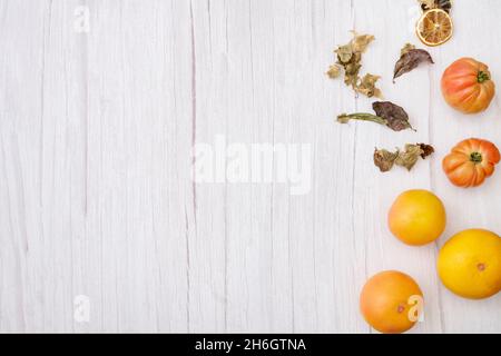 Herbstlicher Fotorahmen mit trockenen Blättern, getrockneten Orangenscheiben, leckeren rosa Tomaten und herzhaften Grapefruits auf weißem Holzbrett, von oben betrachtet Stockfoto