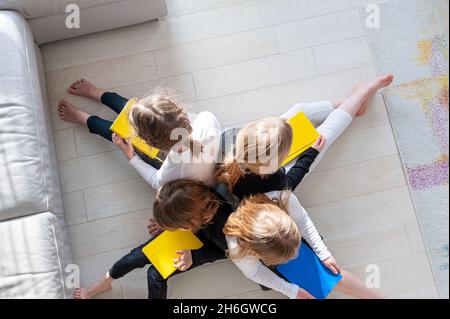 Vier Kinder auf dem Boden im Wohnzimmer, die Vorbereitungsarbeiten für die Schule machen. Gemeinsam lernen. Stockfoto
