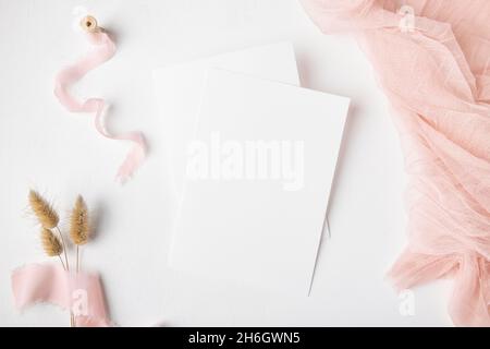 Zwei weiße Hochzeit Einladung Karte mockup auf weißem Tischhintergrund mit rosa Terrakotta-Dekoration und trockenem Gras, minimalistisches mockup 5x7 Verhältnis, ähnlich Stockfoto