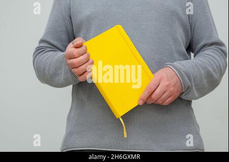 Nahaufnahme im mittleren Abschnitt eines erwachsenen Mannes, der ein gelbes Buch in den Händen hält. Stockfoto