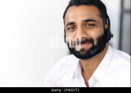 Nahaufnahme eines erfolgreichen bärtigen indianers mit Headset, Experte, Berater oder Operator, schaut direkt auf die Kamera und lächelt freundlich. Support-Servicekonzept, Hotline, Fernkommunikation Stockfoto