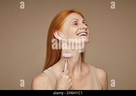 Porträt einer schönen rothaarigen Frau mit Sommersprossen lächeln und tun Gesichtsmassage mit Roller, kopieren Raum Stockfoto