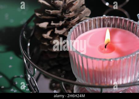 Rosa Duftkerze leuchtet auf einem Spiegeltablett neben Kieferkegel. weihnachtsduft, Wohndekor für den Urlaub Stockfoto