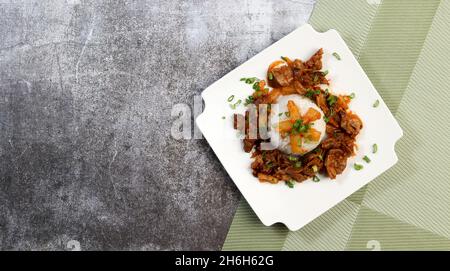 Geschmorte Chicken Gizzards mit gekochtem Reis auf einem quadratischen Teller auf einem dunkelgrauen Hintergrund. Draufsicht, flach liegend Stockfoto