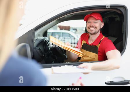 Der fröhliche Arbeiter in der Uniform geben dem Besitzer nach der Adresse das wichtige Paket Stockfoto
