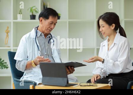 Eine asiatische Patientin konsultiert mit einem Facharzt mittleren Alters zu ihren Verletzungsplänen im Gesundheitszentrum. Stockfoto