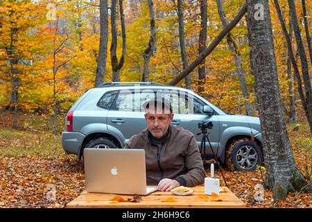 Der Mensch arbeitet am Laptop im Herbstwald Stockfoto