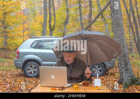 Der Mann arbeitet an regnerischen Tagen im Herbstwald am Laptop Stockfoto