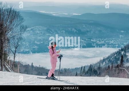 Telefon im Skiurlaub - Frau Skifahrer mit Telefon-App auf der Skipiste Piste in erstaunliche Winter Naturlandschaft. Mädchen, die auf mobile Smartphone tragen Stockfoto