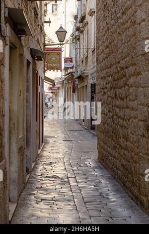 Trogir, Kroatien - 10. November 2021: Enge Gasse mit Kopfsteinpflasterstraße und alten Gebäuden im historischen Stadtzentrum von Trogir Stockfoto