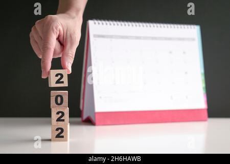 Hand auf 2022 Holzwürfel mit Kalender im Hintergrund. Neues Jahr, neuer Start. Speicherplatz kopieren. Stockfoto