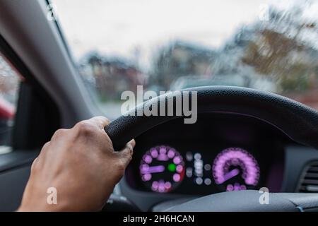 Die Hände des Fahrers auf dem Lenkrad im Inneren eines Fahrzeugs. Fahren an einem regnerischen Tag. Stockfoto