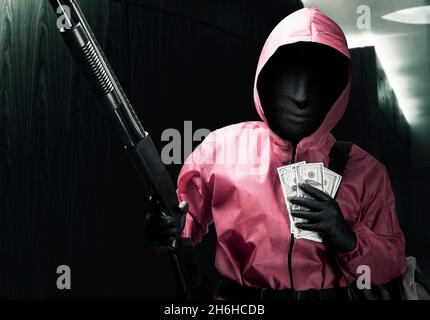 Krimineller Mann in rosa Uniform und einer versteckten Maske, die die Schrotflinte hält und nach dem Raub eine Tasche mit Geld in der Hand hat Stockfoto