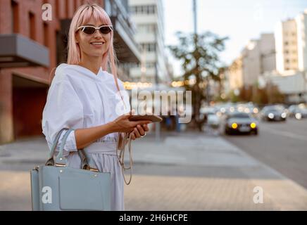 Fröhliche Frau, die auf der Straße steht und das Handy hält Stockfoto