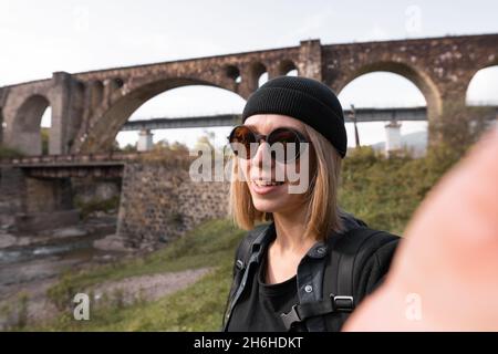 Eine Bloggerin, die eine Live-Übertragung der alten Bogensteinbrücke der Eisenbahn leitet, eine Touristin auf einer Reise, die einen Videoblog über Brücken führt Stockfoto