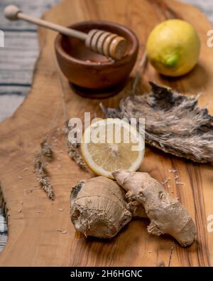 Zusammensetzung aus Ingwerwurzeln, Zitronen und Honig mit Honigstreuer auf einem hölzernen Schneidebrett Stockfoto