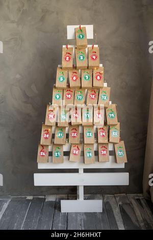 Handgefertigte Adventskalender Geschenke in Basteltaschen hängen auf einem hölzernen Weihnachtsbaum. Kreatives Geschenk mit Zahlen für Kinder für das neue Jahr Stockfoto