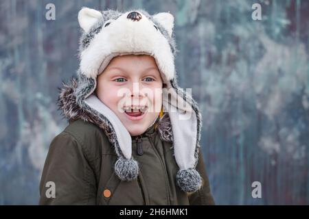 Porträt eines überraschten Kindes in einem Wolfhut und lächelt süß auf grauem Hintergrund, draußen. Platz für Text. Hochwertige Fotos Stockfoto