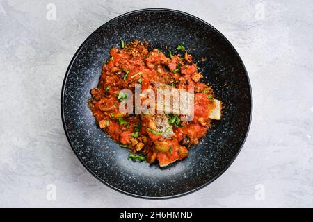 Draufsicht auf gerösteten Zander, serviert mit gedünsteter Tomate, Zwiebel und Olivensoße auf einem Teller Stockfoto