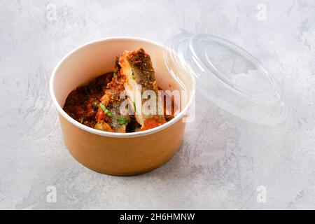 Gerösteter Zander mit gedämpfter Tomate, Zwiebel und Olivensoße in Papppackage zum Mitnehmen Stockfoto