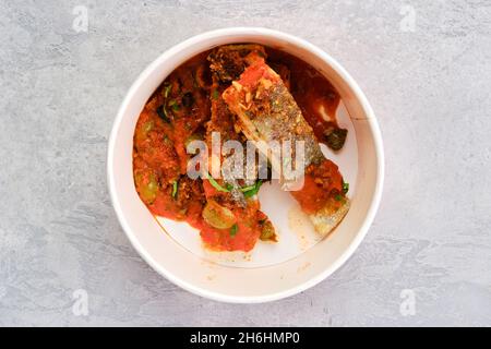 Draufsicht auf gerösteten Zander, serviert mit gedünsteter Tomate, Zwiebel und Olivensoße in Papppackung zum Mitnehmen Stockfoto