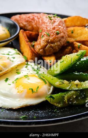 Nahaufnahme von Spiegeleiern mit Wurst, Kartoffelkeilen und eingelegter Gurke Stockfoto