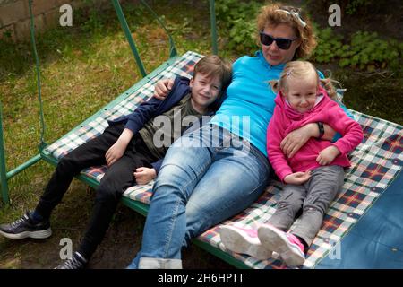 Großmutter und ihre zwei Enkelkinder, die Spaß auf einer Schaukel haben, Enkel und Enkelin lieben ihre Oma. Entspannende Outdors in Oma Landschaft Hou Stockfoto