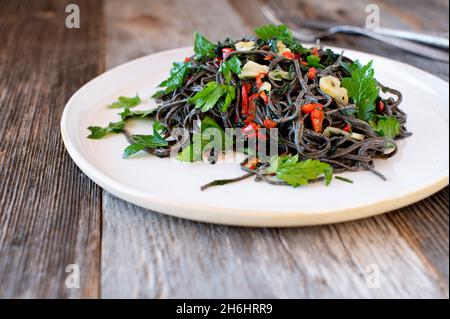 Glutenfreie und proteinreiche Linsennudeln mit Olivenöl, Knoblauch und Chili al olio. Serviert auf einem Teller mit Parley Stockfoto