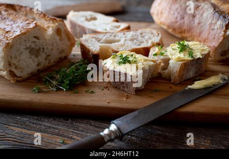 Französisches Baguette in Butterscheiben auf einem rustikalen, hölzernen Schneidebrett mit Messer Stockfoto