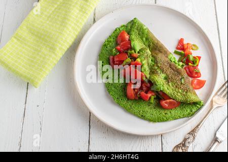 Grünes Omelett mit Eiern und Spinat, serviert mit einem Tomto-Salat auf einem Teller Stockfoto