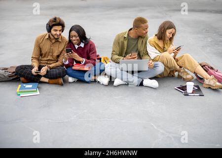 Studenten sitzen und mit Smartphones auf Asphalt Stockfoto