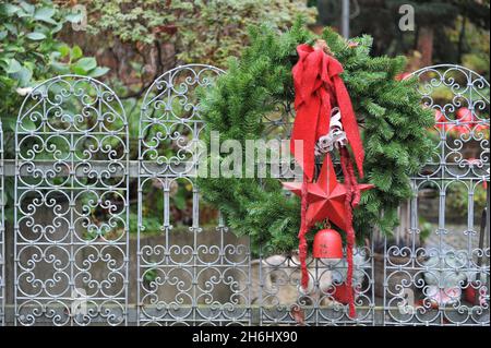 Winterdekoration im Garten. Ein Tannenweihnachtskranz mit rotem Bogen, Stern und Glocke auf einem metallischen Gartentor Stockfoto