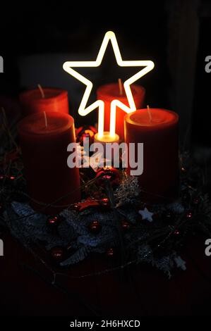 Weihnachtliche Dekoration im Innenraum. Ein Adventskranz mit vier roten Kerzen und einem Lichtstern in Dunkelheit Stockfoto