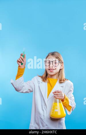 Schülerin hält chemischen Behälter und Reagenzglas trägt Schutzkleid und Brille auf blauem Hintergrund mit leerem Platz für Text Stockfoto