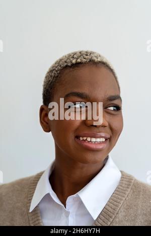 Positive afroamerikanische in stilvollem Outfit und mit gefärbten kurzen Haaren mit charmantem Lächeln auf weißem Hintergrund im Studio Stockfoto