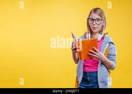 Happy Teenager Mädchen hält Rucksack Buch zu lesen. Studio-Hochformat auf gelbem Hintergrund mit Leerzeichen für Text. Stockfoto