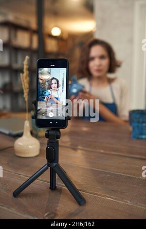 Smartphone mit junger Handwerkerin auf dem Bildschirm geben Meisterkurs für diejenigen, die handgemachte Keramik machen will Stockfoto