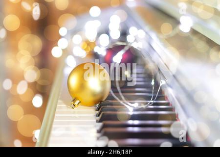 Weihnachtliche goldene Kugel mit Girlande auf Klavier auf Bokeh-Hintergrund. Musikkonzept für Neujahr oder Weihnachten. Weichfokus Stockfoto