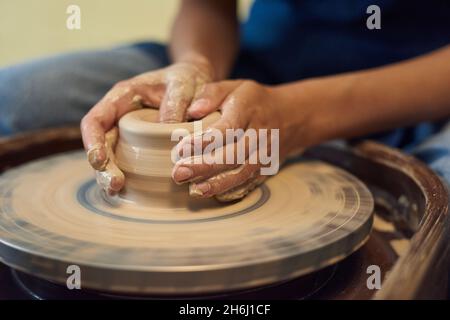Hände von jungen Handwerkern halten durch Drehen Töpferscheibe während der Arbeit über neue handwerkliche Tonwaren in der Werkstatt Stockfoto