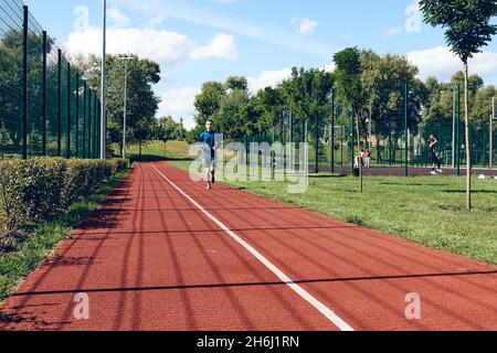 Sportlicher junger Mann beim Laufen. Trainieren, Stretching im städtischen Bereich oder Park am Morgen. Selbstpflege authentisch, Wellness- und Sportkonzepte Stockfoto