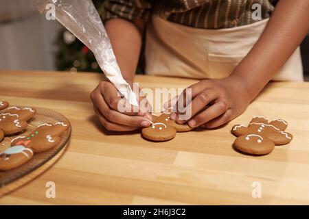 Hände von afrikanischen Mädchen Dekoration hausgemachten Lebkuchen mit weißer Glasur, während sie von Holztisch stehen Stockfoto