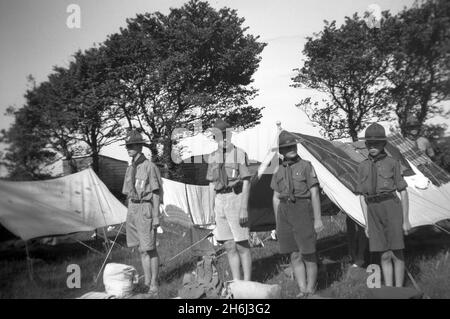 1938, historisch, Pfadfinderlager, außerhalb ihrer Zelte, eine Hirteninspektion, Pfadfinder stehen in ihrer Uniform und Pfadfindermützen, Ringmore, Devon, England, Großbritannien, Ein Hirsch oder Pfadfinder Patrouille ist traditionell ein kleines Team von Pfadfinder, die Fähigkeiten, Verantwortlichkeiten und Führung erlernen. Die Pfadfinderungsversuche begannen 1908, nachdem Robert Baden-Powell, ein britischer Armeeoffizier, im vergangenen Sommer ein Versuchslager auf Brownsea Island, Poole Harbour, abhielt. Rund 20 Jungen nahmen an einer Reihe von Outdoor-Fähigkeiten Teil und wurden ihnen beigebracht. Baden-Powell's berühmtes und meistverkauftes Buch, „Scouting for Boys“, wurde erstmals 1908 veröffentlicht. Stockfoto