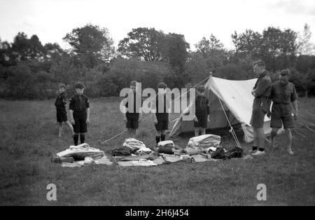 1938, draußen auf einem Feld neben ihrem Zelt, findet eine Kit-Inspektion von Jungen Scouts statt, Felbridge, Surrey, England, Großbritannien. Die Pfadfinderungsversuche begannen 1908, nachdem General Robert Baden-Powell, der britische Armeeoffizier, im vergangenen Sommer ein Versuchslager auf Brownsea Island, Poole Harbour, abhielt. Rund 20 Jungen nahmen an einer Reihe von Outdoor-Fähigkeiten Teil und wurden darin unterrichtet, darunter Tracking, Feuerbekämpfung, das Herstellen von Unterständen aus Ästen, Knüpfen, Kochen, Gesundheit und Hygiene, lebensrettende Maßnahmen und erste Hilfe. 1914 wurden Junge Pfadfinder oder Wolf Cubs für Jungen im Alter von neun Jahren ins Leben gerufen. Im Alter von 12 Jahren konnten sie zu Pfadfindern werden. Stockfoto