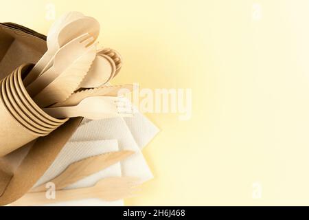 Draufsicht auf Öko Geschirr auf beigefarbenem Hintergrund mit Kopierfläche. Basteln Sie Teller, Kaffeetassen, Bambuslöffel, Gabeln, Messer und Servietten. Stockfoto