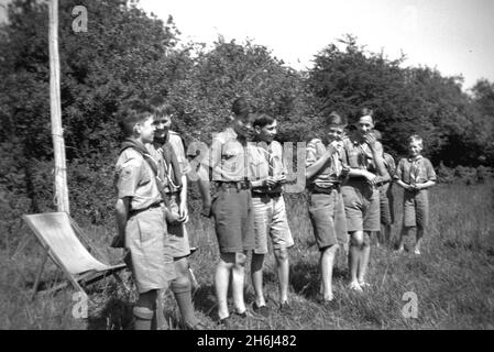 1939, draußen auf einem Feld, lachen die Jungen der 13. Purley Scouts in ihren Uniformen gemeinsam im Lager für die Adkin Challenge Trophy, England, Großbritannien. Die Pfadfinderungsversuche begannen 1908, nachdem General Robert Baden-Powell im vergangenen Sommer ein Versuchslager auf Brownsea Island, Poole Harbour, abgehalten hatte. Rund 20 Jungen nahmen daran Teil und lernten eine Reihe von Outdoor-Fähigkeiten, darunter Tracking, Feuerbekämpfung, das Herstellen von Unterständen aus Ästen, Knüpfen, Kochen, Gesundheit und Hygiene, lebensrettende und erste Hilfe. Baden-Powell's berühmtes Buch, 'Scouting for Boys', wurde 1908 veröffentlicht. Stockfoto